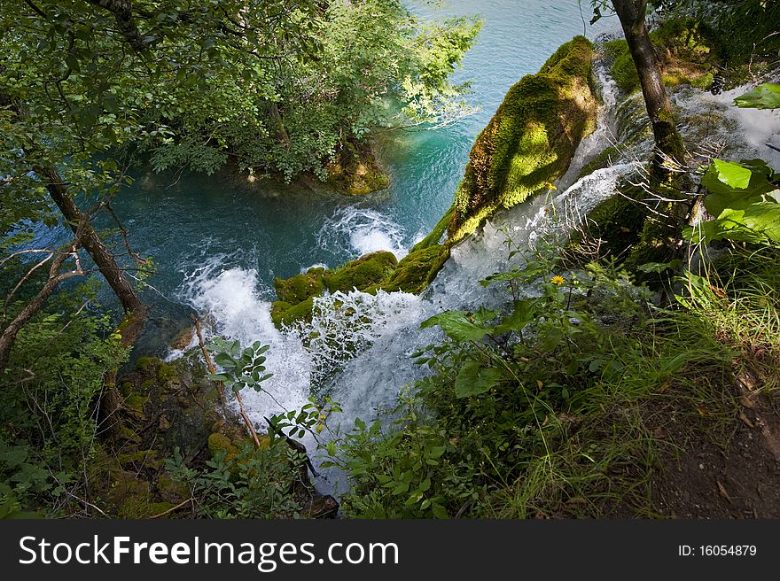 Waterfall and green water of Plitvice lakes viewed through trees