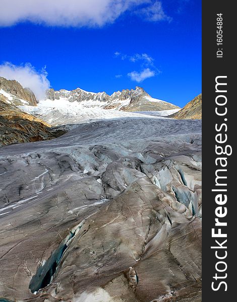 A Glacier showing a crack with snow covered mountains under a blue sunny sky and clouds. A Glacier showing a crack with snow covered mountains under a blue sunny sky and clouds