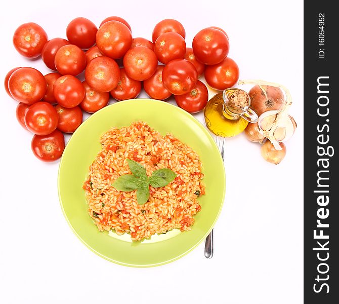 Risotto with tomatoes on a green plate decorated with basil with fresh tomatoes, onions, garlic and olive oil on white background