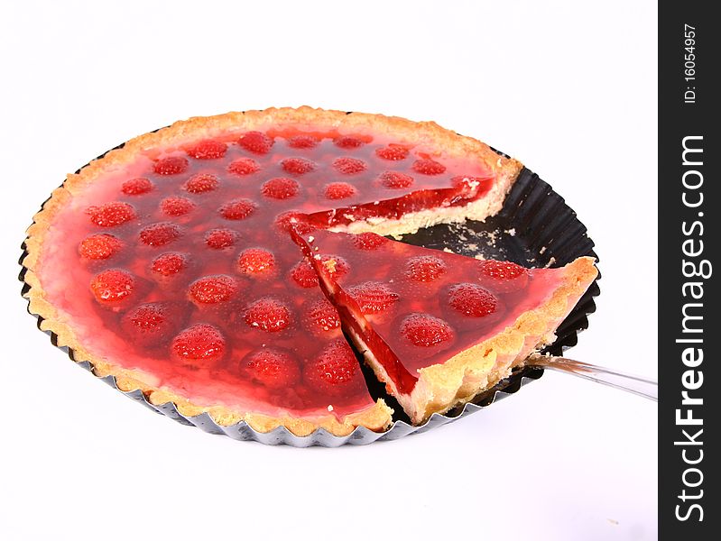 Strawberry Tart in a tart pan with a slice of it cut out on a white background