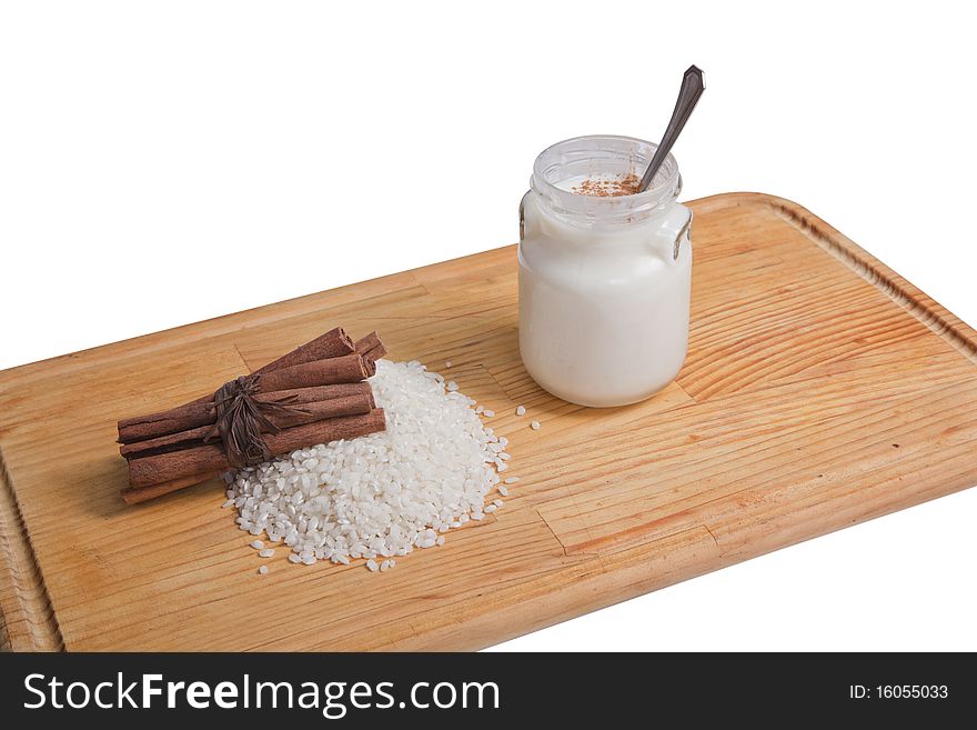 Tub of rice pudding and cinnamon on wooden board, accompanied by a handful of rice and cinnamon, isolated white background