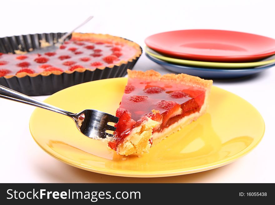 Piece of Strawberry Tart on a yellow plate a tart panand plates in the background and some of the tart on a fork