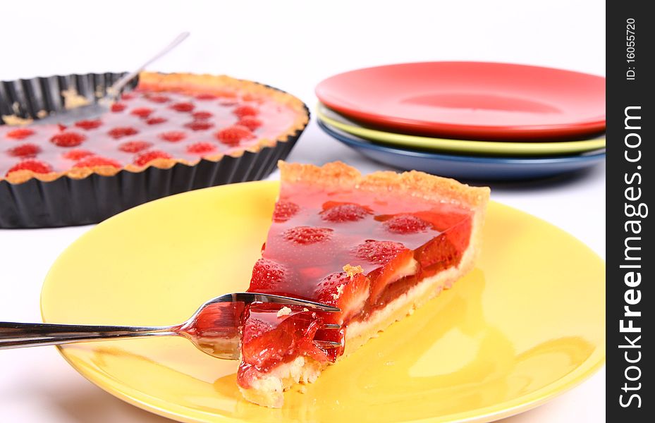 Piece of Strawberry Tart on a yellow plate being eaten with a fork, a tart pan and plates in the background