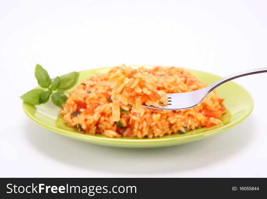 Risotto with tomatoes on a green plate decorated with basil being eaten with a fork