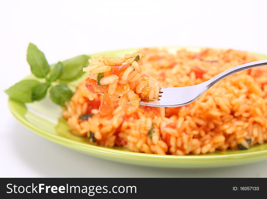 Risotto with tomatoes on a green plate decorated with basil being eaten with a fork