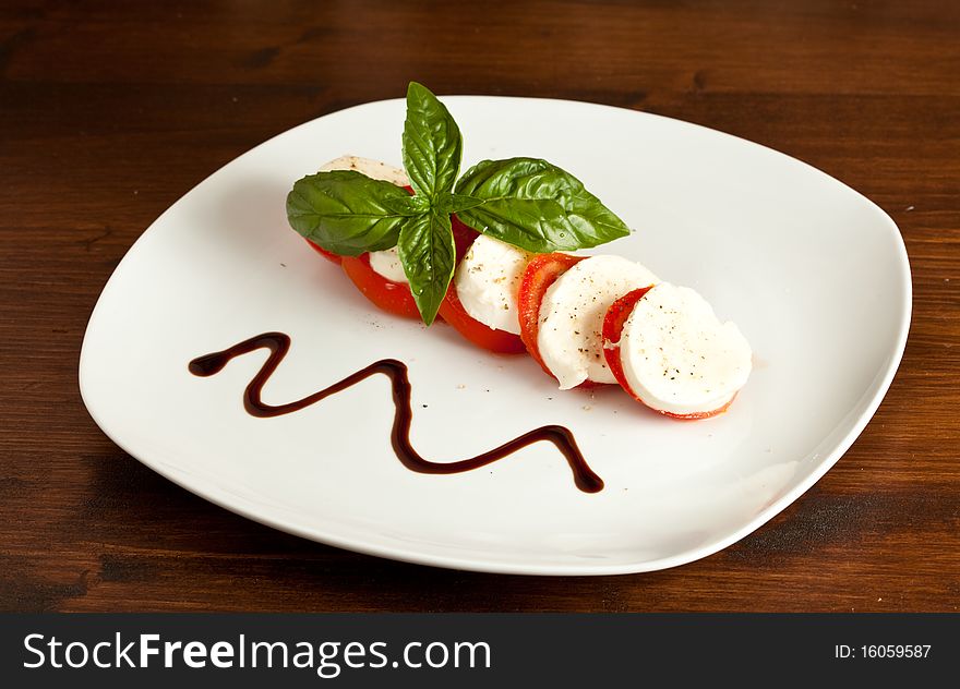 Italian caprese made of tomato, mozzarella and basil putted on a wood table. Italian caprese made of tomato, mozzarella and basil putted on a wood table