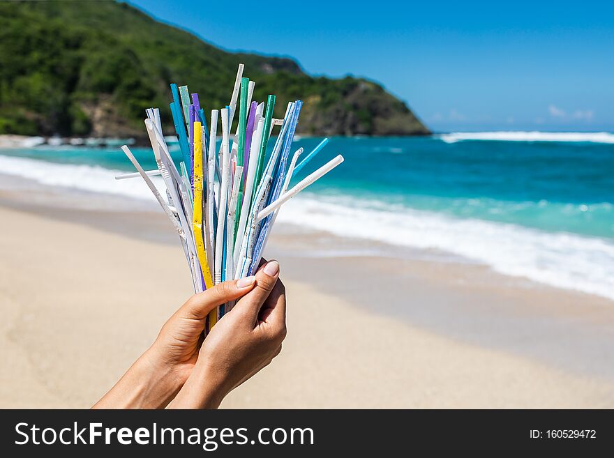 Hand holding heap of plastic straws on ocean beach