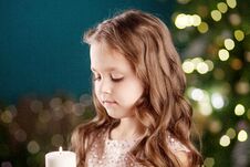 Portrait Of Acute Long-haired Little Girl In Dress On Background Of Lights.Little Girl Holding Burning Candle. Christmas, New Stock Images Portrait Of Acute Long-haired Little Girl In Dress On Background Of Lights.Little Girl Holding Burning Candle. Christmas, New Stock Images