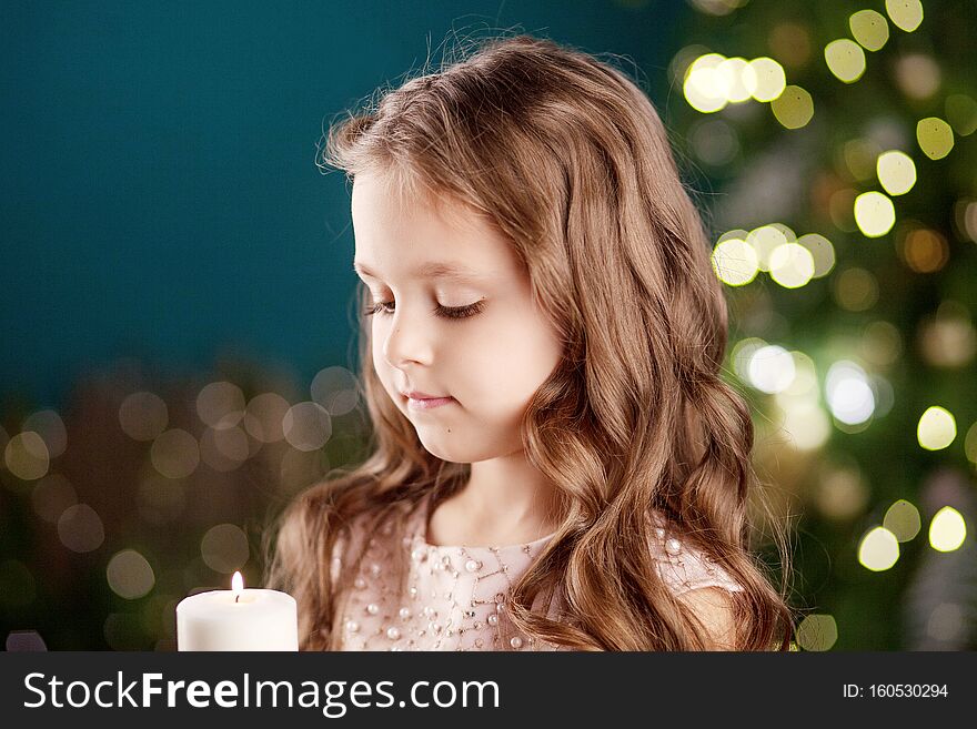 Portrait of acute long-haired little girl in dress on background of  lights.Little girl holding burning candle. Christmas, New
