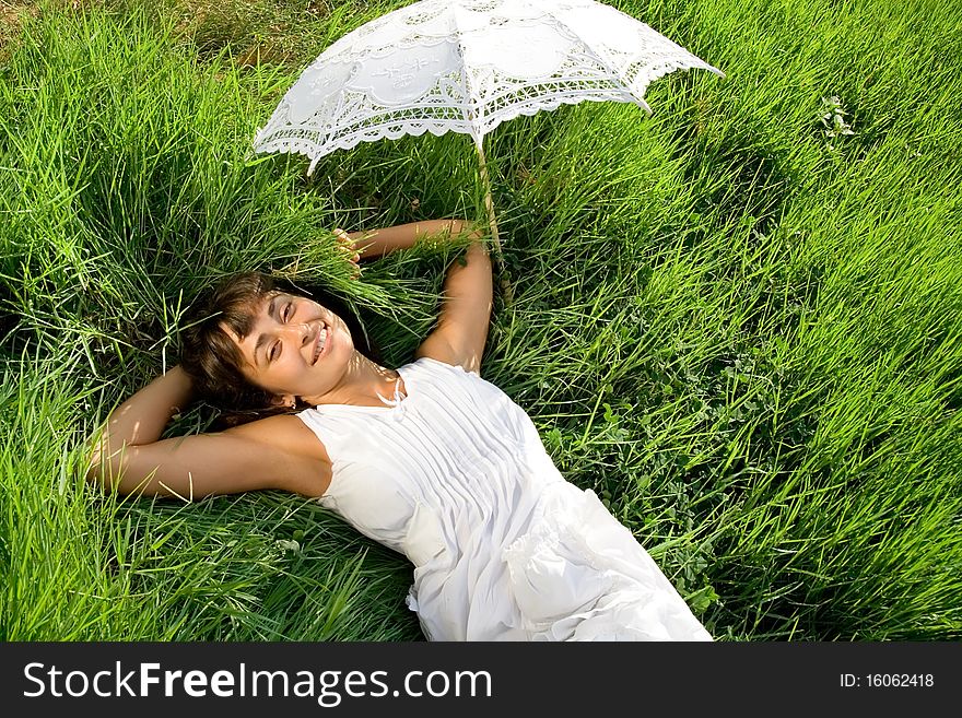 Young pretty lady in white dress and with umblella having a rest on the green meadow. Young pretty lady in white dress and with umblella having a rest on the green meadow