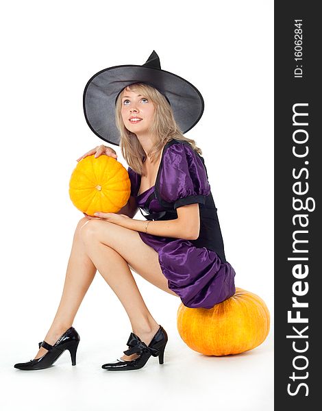 Young blonde witch sitting on a pumpkin, holding a pumpkin