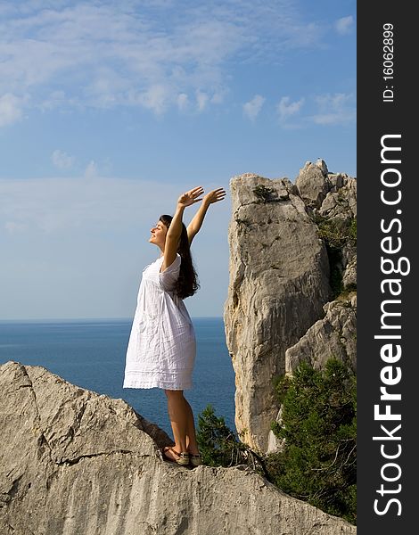 Happy young girl standing on the rocks with her hands up with the sea as a background