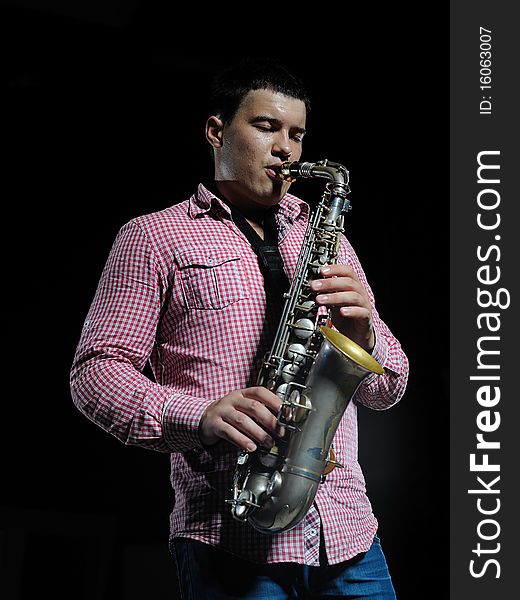 Young handsome man playing music on saxophone. black background