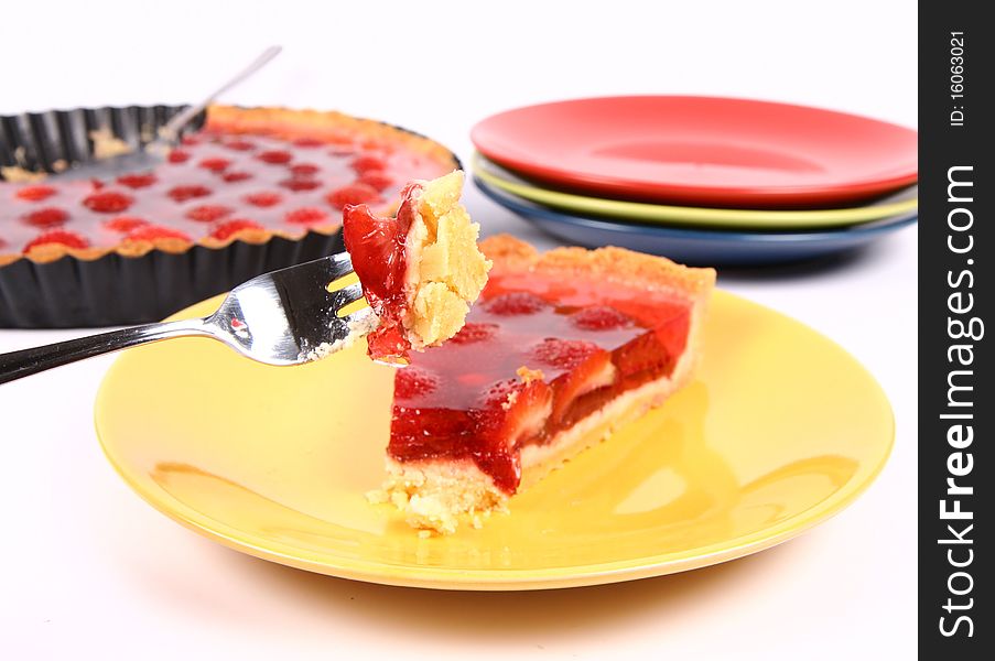 Piece of Strawberry Tart on a yellow plate, a tart pan and plates in the background, and some of the tart on a fork