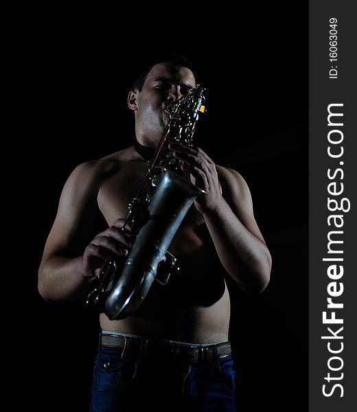 Young handsome man playing music on saxophone. black background