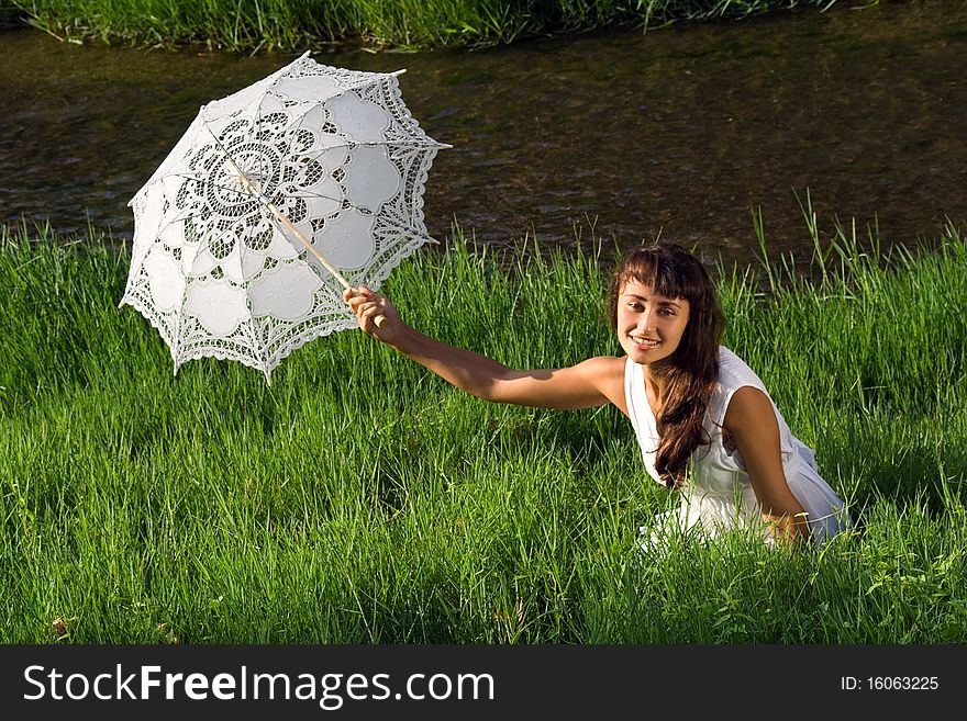 Young beautiful girl in white with sun umbrella sitting in the fresh green grass near the river. Young beautiful girl in white with sun umbrella sitting in the fresh green grass near the river