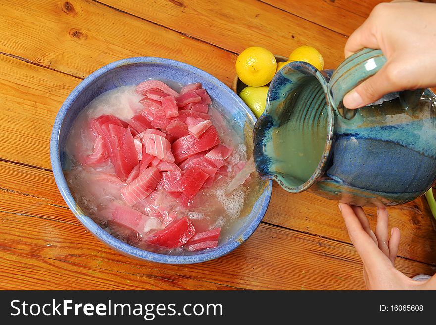Pouring lemon juice to marinating tuna fish. Pouring lemon juice to marinating tuna fish