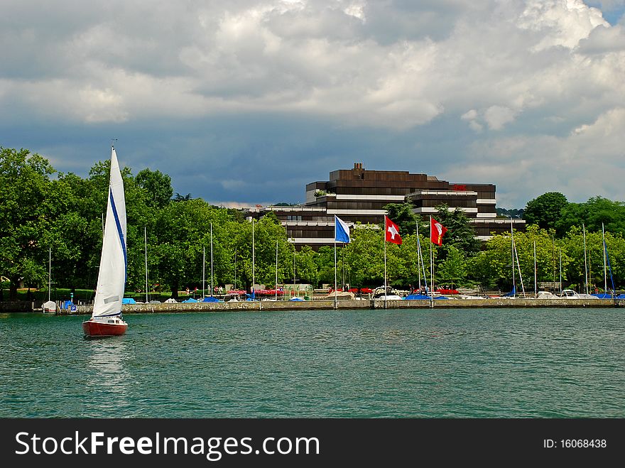 Sailboat coming from Zurich yachtport, deep turquoise water of the zurich lake and some yachts are at foreground and the sky conered with rainy clouds is at background