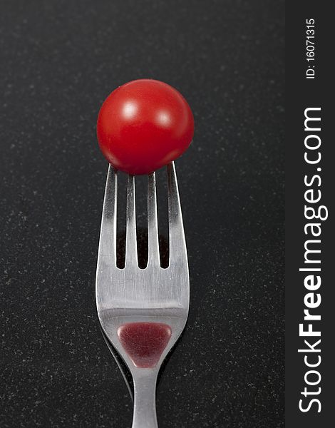 Tomato on a fork with reflection. On a black granite counter. Note: Differential focus.