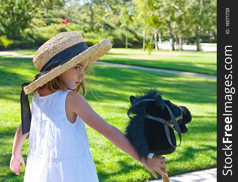 Little girl wearing straw hat and holding her toy pony. Little girl wearing straw hat and holding her toy pony