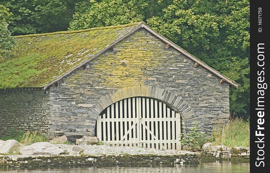 An image of a boat house with arched doorway and slatted wooden doors situated on an English lakeside. An image of a boat house with arched doorway and slatted wooden doors situated on an English lakeside.