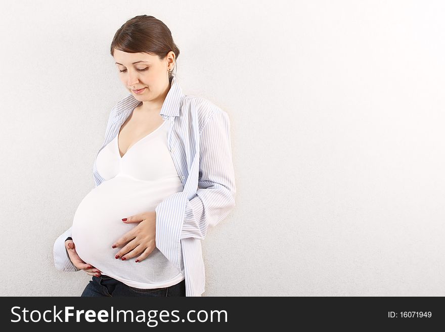 Happy pregnant woman in white near the wall