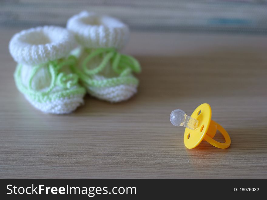 Baby's bootees and yellow pacifier. Baby's bootees and yellow pacifier