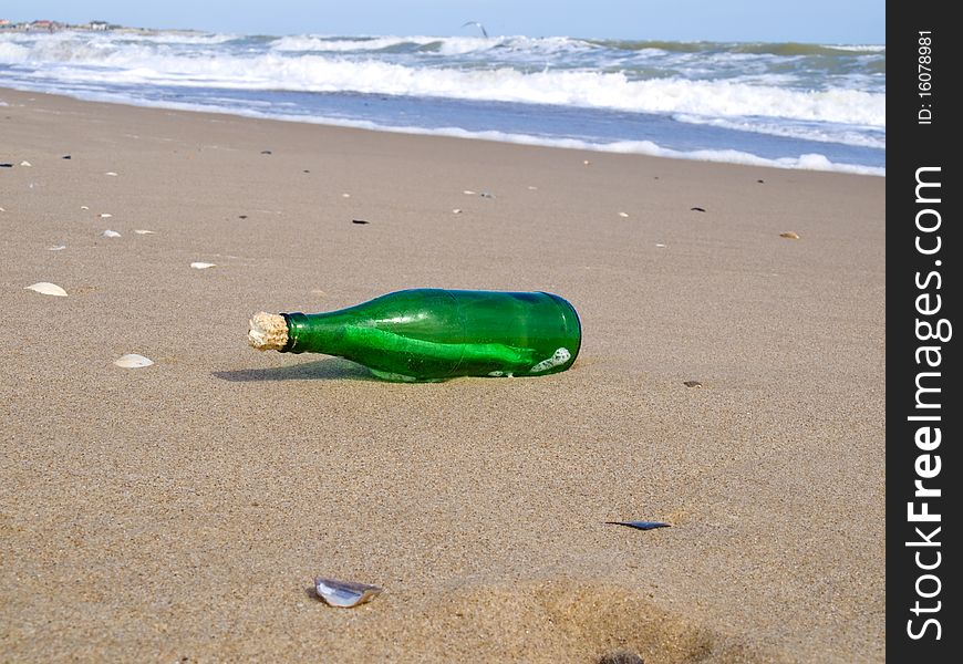 The closed bottle of green color with a note in it lies on seacoast on sand. The closed bottle of green color with a note in it lies on seacoast on sand