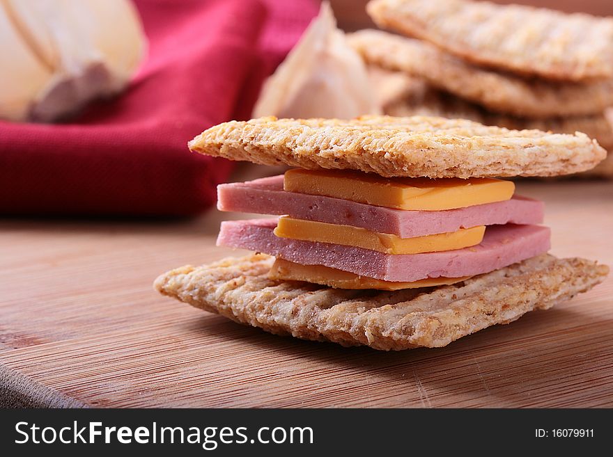 Wheat crackers on a kitchen board with cheese and bologna.