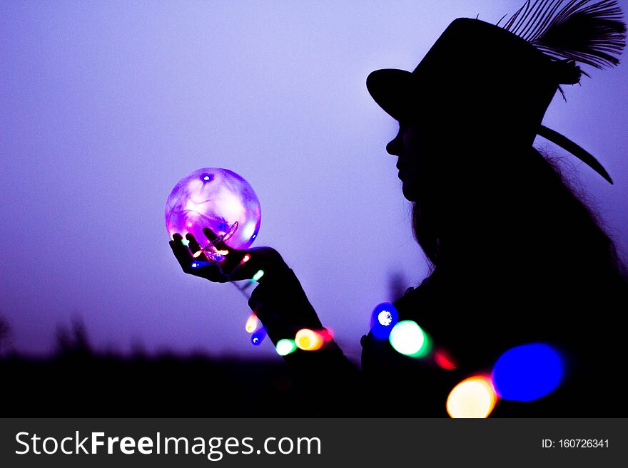 The silhouette of a woman in a high hat with a glowing ball in her hands