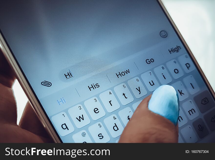 Female hand with blue nails is typing on a white smartphone a message.