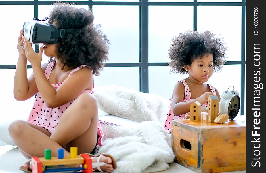 Soft blur image of one African mixed race girl enjoy with VR glasses while the other girl as main focus subject  play with some toys and they sit on floor.