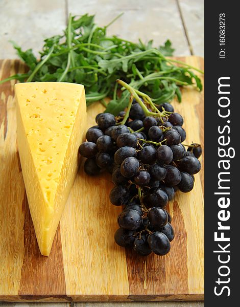 Black grapes and cheese with herbs on a wooden board