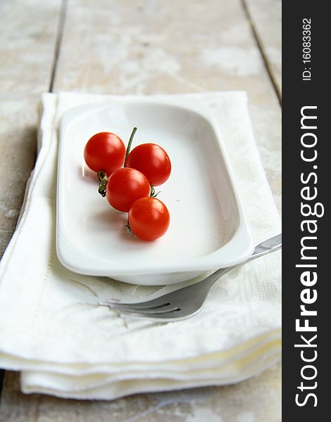 Sprig of cherry tomatoes on a white plate with a white napkin on the table. Sprig of cherry tomatoes on a white plate with a white napkin on the table