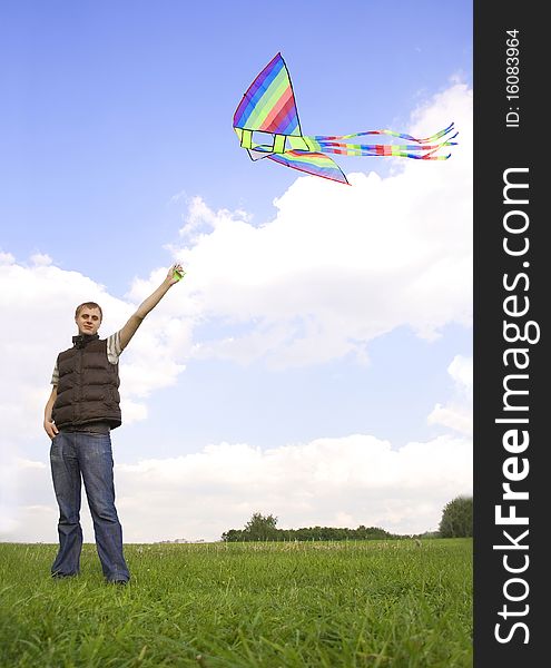 Young man standing on summer lawn and playing with multicolored kite, looking at camera. Young man standing on summer lawn and playing with multicolored kite, looking at camera