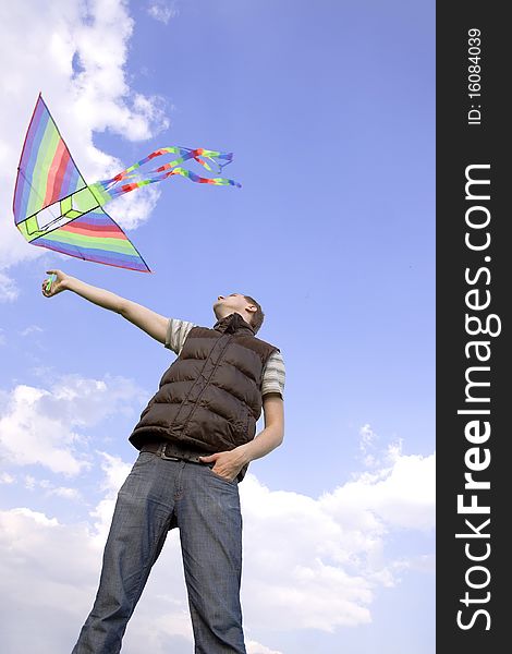 Young man playing with multicolored kite and looking on it, view from below