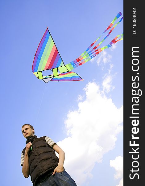 Young man playing with multicolored kite and looking at side, view from below