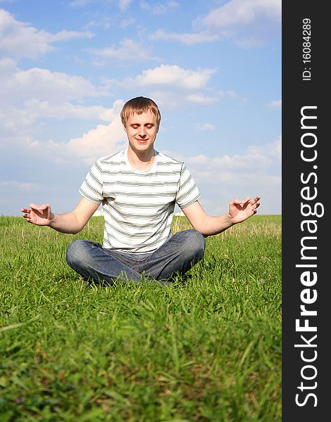 Young handsome man sitting on green summer lawn and meditating with closed eyes. Young handsome man sitting on green summer lawn and meditating with closed eyes