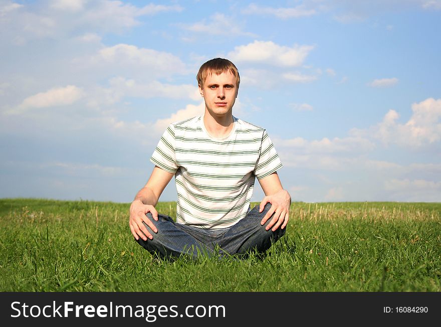 Young man in jeans and white shirt with stripes siting at summer lawn, hands on knees, looking at camera. Young man in jeans and white shirt with stripes siting at summer lawn, hands on knees, looking at camera