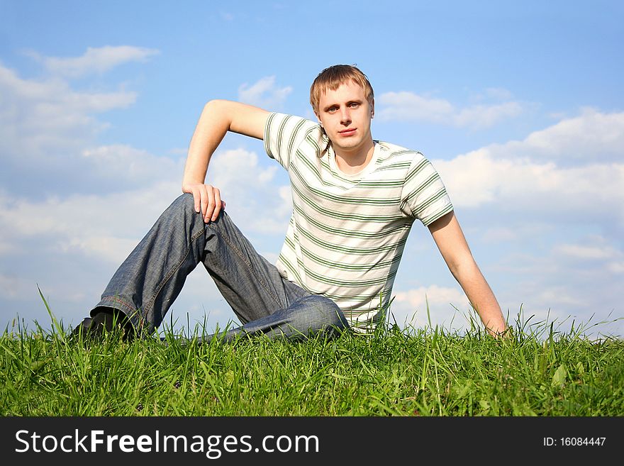 Young handsome man siting on summer lawn, hand on knee, looking at camera