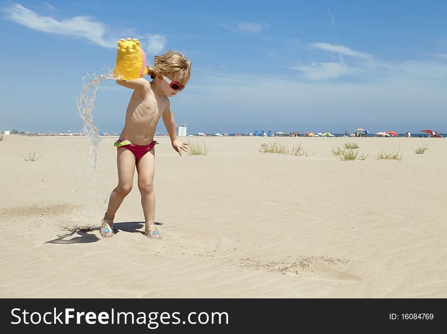 Small blond girl playing and splashing water in the beach on a summer day. Small blond girl playing and splashing water in the beach on a summer day