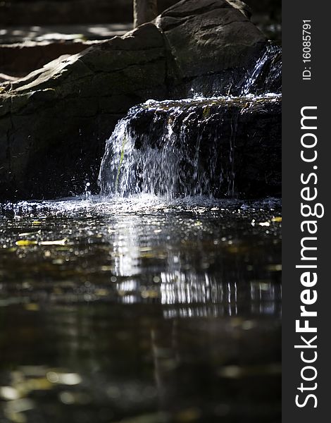 A sunlit waterfall and reflection into a calm pool against a rock background