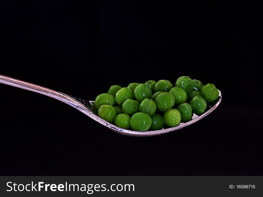 Fresh Sweet Peas on a spoon against a black background