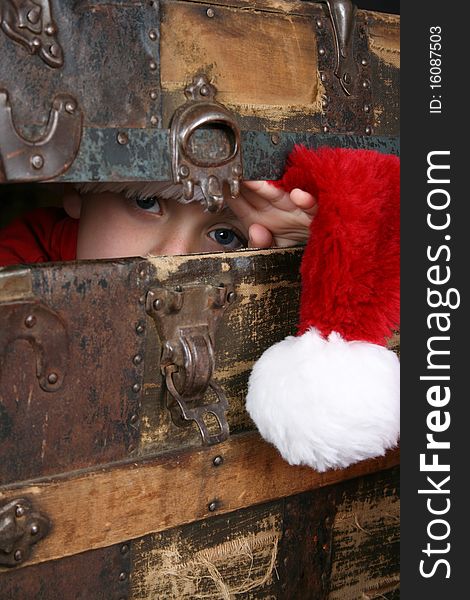 Serious boy with a christmas hat peeping from inside an antique trunk. Serious boy with a christmas hat peeping from inside an antique trunk