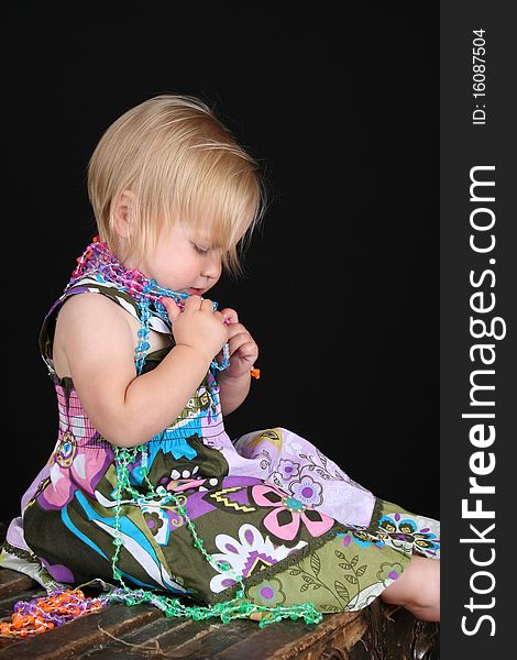 Beautiful blond toddler sitting on an antique trunk playing with beads. Beautiful blond toddler sitting on an antique trunk playing with beads