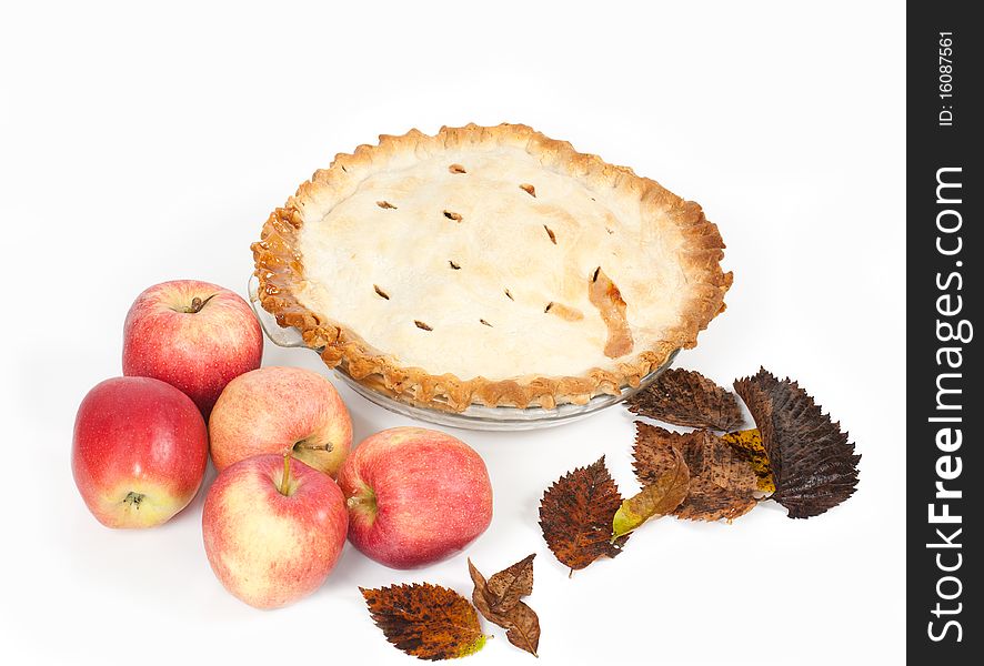 A 100mm macro angled studio shot of a homemade apple pie with apples and autumn leaves on a white background. A 100mm macro angled studio shot of a homemade apple pie with apples and autumn leaves on a white background.