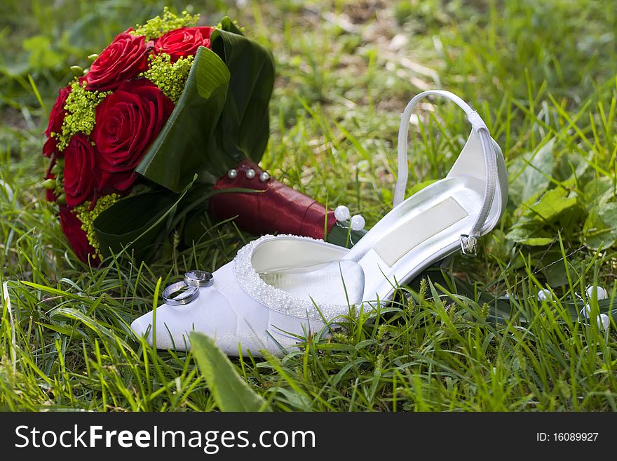 Wedding symbols in the grass. Rings, bouquet and white high heel shoe.