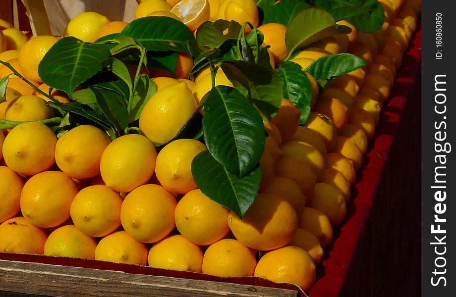Fresh bright yellow lemons and green leaves on display at market place on old wooden table in bright sunlight with strong shadows. organic and healthy food concept.