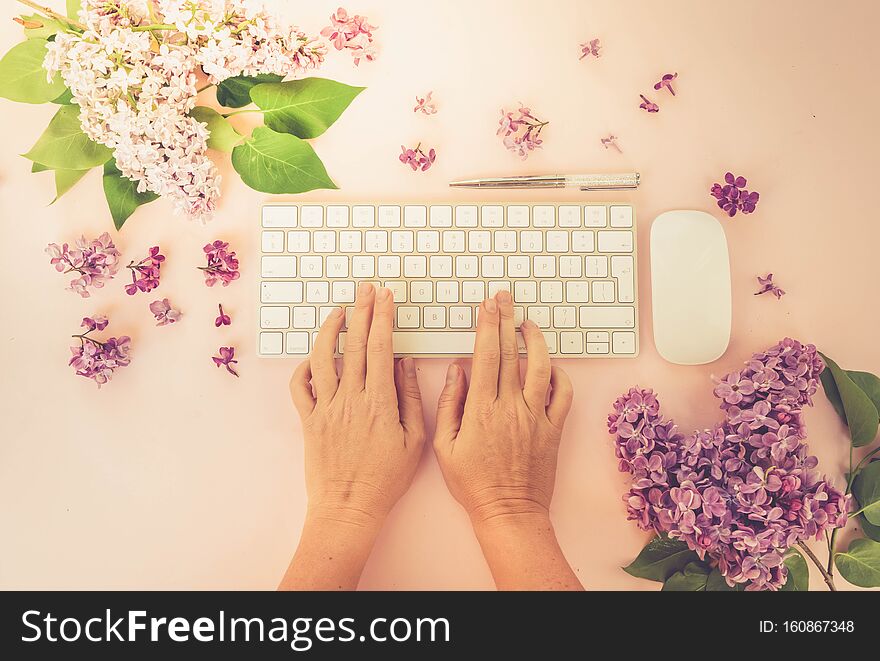 Flat lay home office workspace - modern keyboard with two hands typing, fresh lilac flowers, toned. Flat lay home office workspace - modern keyboard with two hands typing, fresh lilac flowers, toned