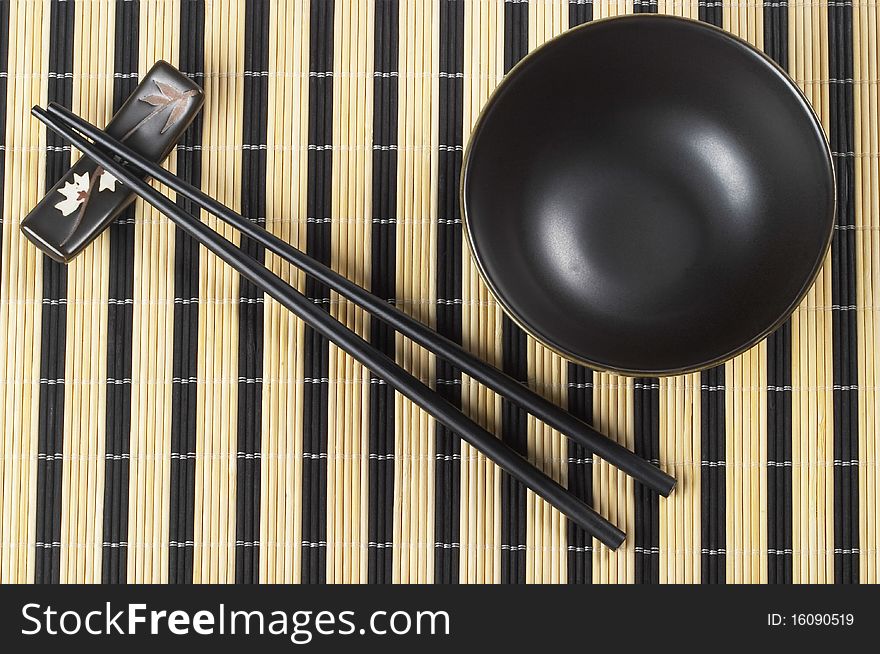 Wooden chopsticks and little ceramic bowl on the bamboo mat background. Wooden chopsticks and little ceramic bowl on the bamboo mat background